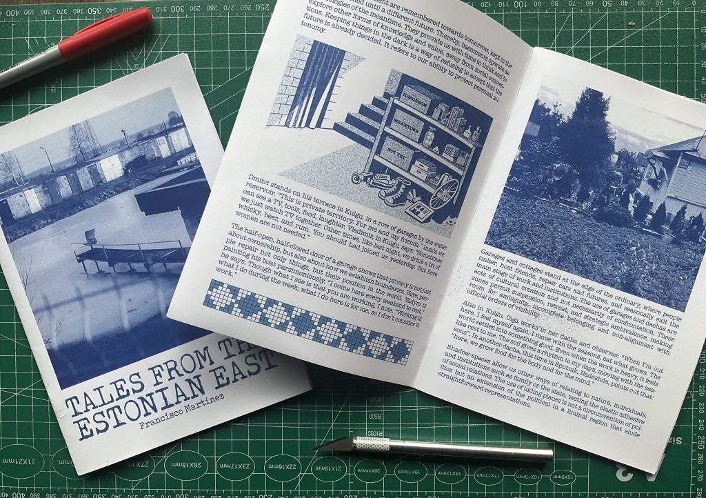 Several blue-toned pages are spread out on a cutting mat, featuring a pen and craft knife, with photos, illustrations, and text layouts.